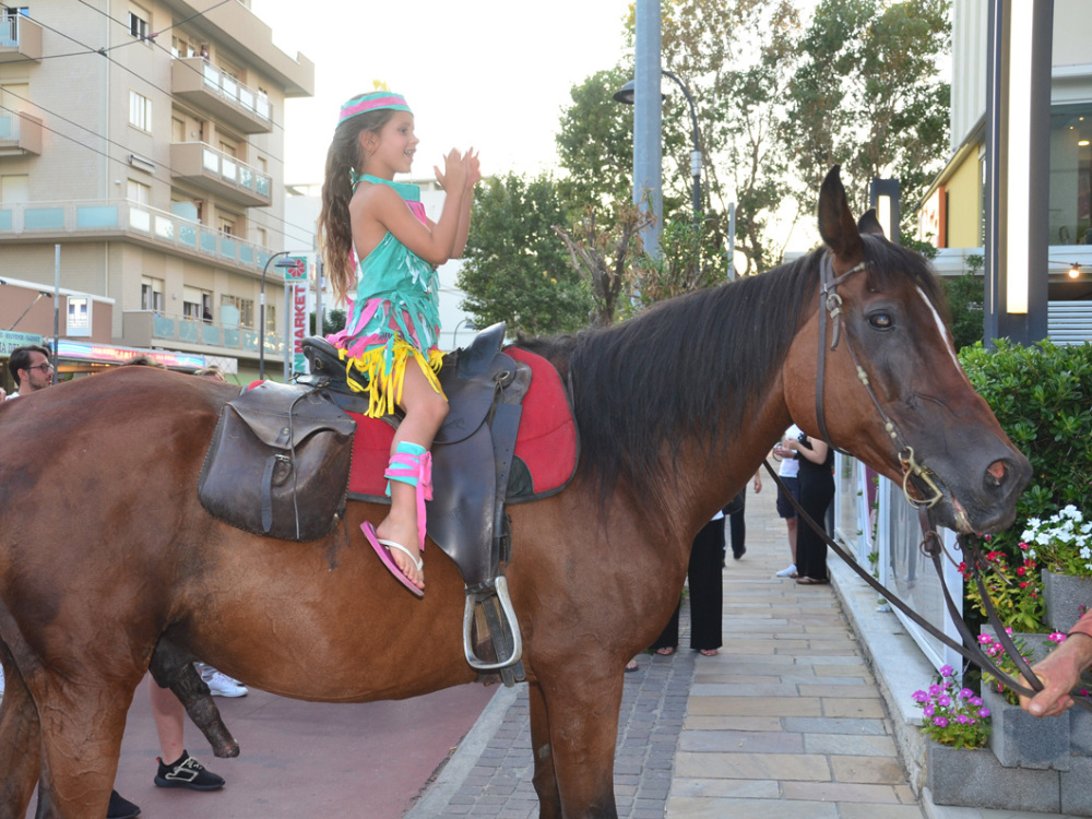 Bambina in costume colorato su cavallo in città.