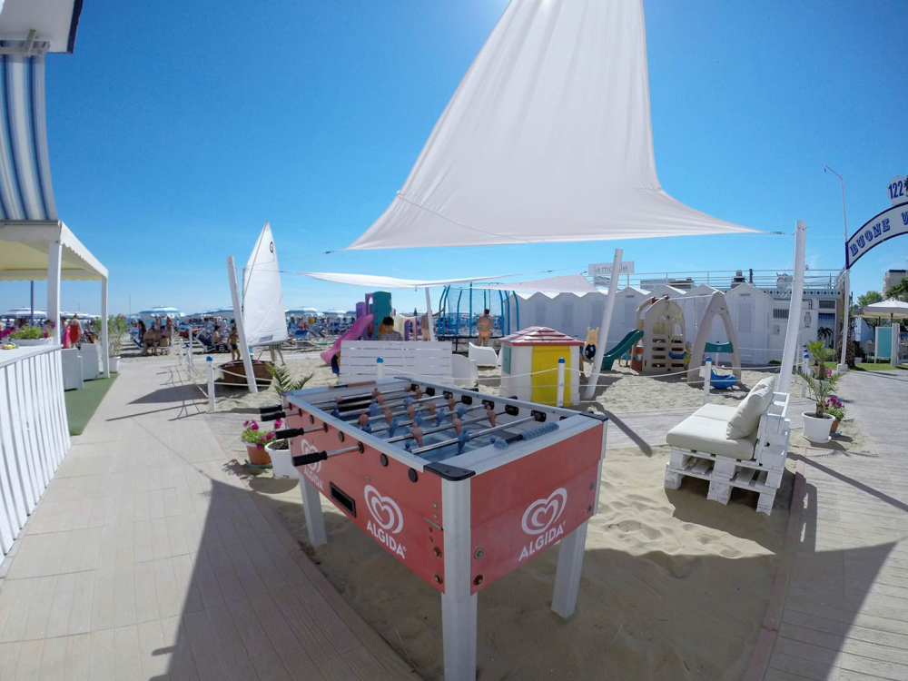 Spiaggia con giochi, calcetto Algida e area relax sotto il sole estivo.