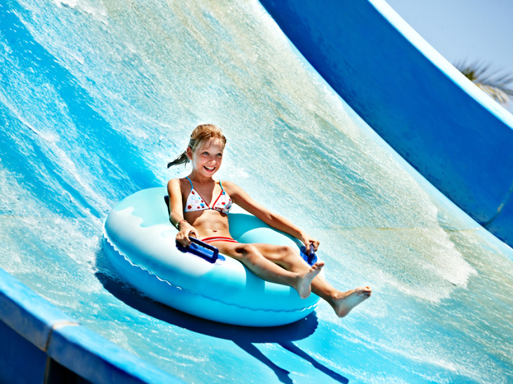 Bambina su scivolo d'acqua con ciambella blu in un parco acquatico.