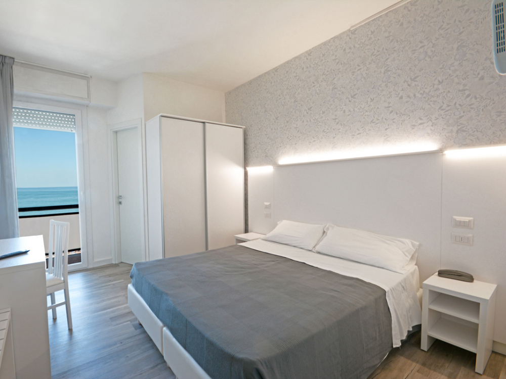 Camera moderna con vista mare, letto matrimoniale e arredi bianchi.