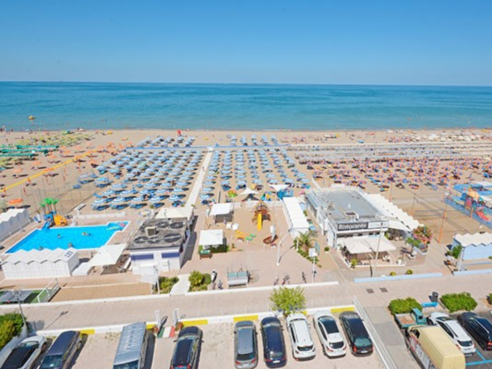 Spiaggia affollata con lettini, ombrelloni e vista mare, piscina e ristorante vicini.