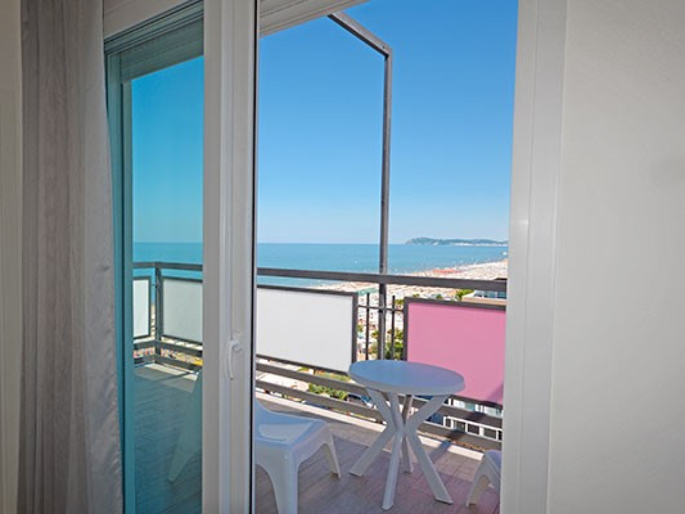 Vista mare da un balcone con tavolino e sedie, cielo sereno.