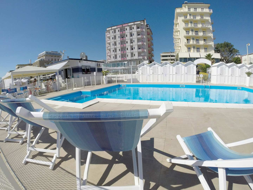 Piscina all'aperto con lettini e cabine bianche.