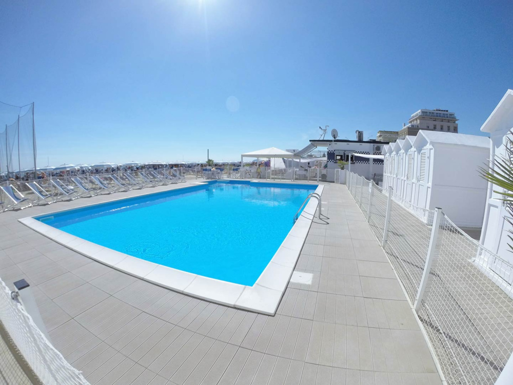 Piscina all'aperto con lettini e cabine bianche al sole.