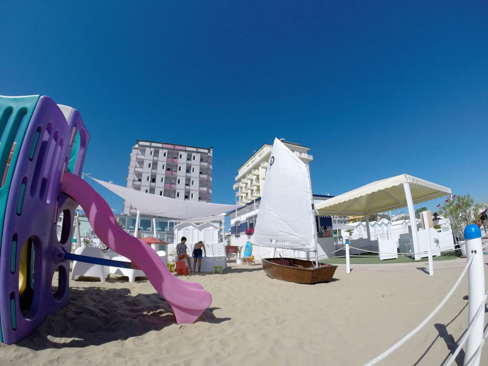 Spiaggia con scivolo e barca a vela, giornata soleggiata.
